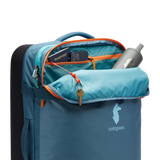 Cotopaxi 65L Roller Bag checked luggage with durable wheels and handle, blue color, ready for travel and easy to maneuver.