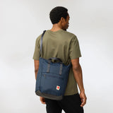 Fjallraven High Coast Totepack in black, showcasing its compact design, top handles, adjustable shoulder strap, and exterior zip pocket.