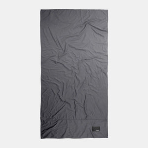Charcoal Matador Nanodry packable beach towel folded and spread out, showcasing its lightweight, quick-drying fabric and compact design.