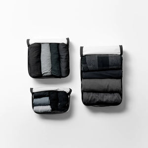 Set of three white Matador packing cubes with multiple compartments for organized travel storage, shown in a 19-piece travel set.