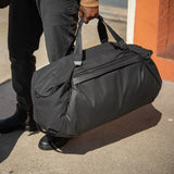 Black Peak Design Travel Duffel 65L with multiple handles, side zipper compartments, and adjustable shoulder strap for travel.