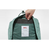 Fjallraven Kanken backpack in frost green with top handle and adjustable shoulder straps, featuring a front zip pocket and main compartment.