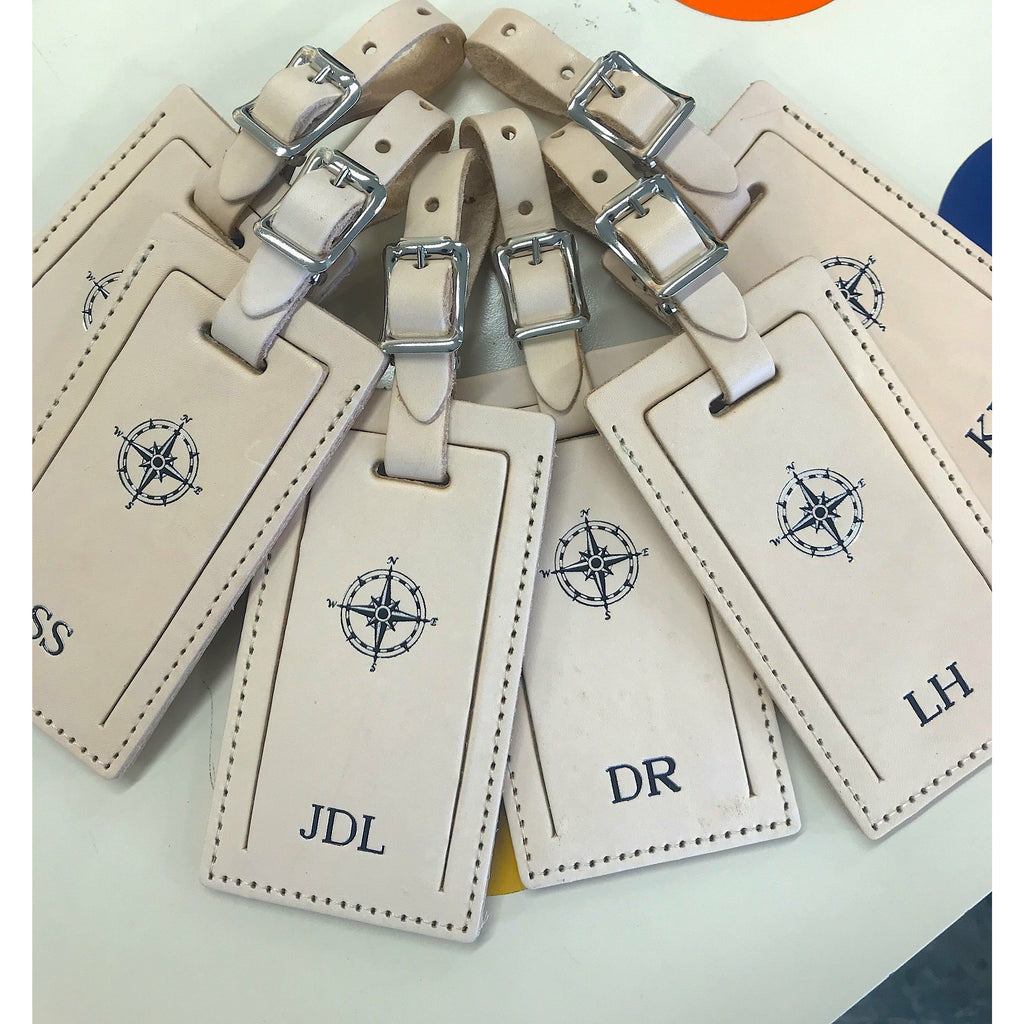 Personalized leather luggage tag by Index Urban with embossed name, made in USA, attached to a suitcase for travel identification.