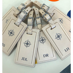 Personalized leather luggage tag by Index Urban with embossed name, made in USA, attached to a suitcase for travel identification.