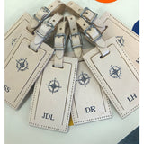 Personalized leather luggage tag by Index Urban with embossed name, made in USA, attached to a suitcase for travel identification.