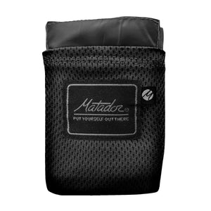 Matador Pocket Blanket 2.0 in black, compact outdoor accessory with a foldable design and carrying case on white background.